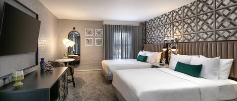 A hotel room with two beds, a desk, a TV, and a patterned wall.