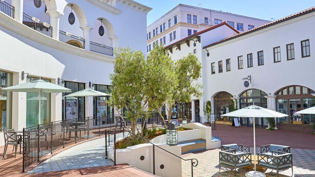 A courtyard with outdoor seating, a fountain, and white buildings with arches.