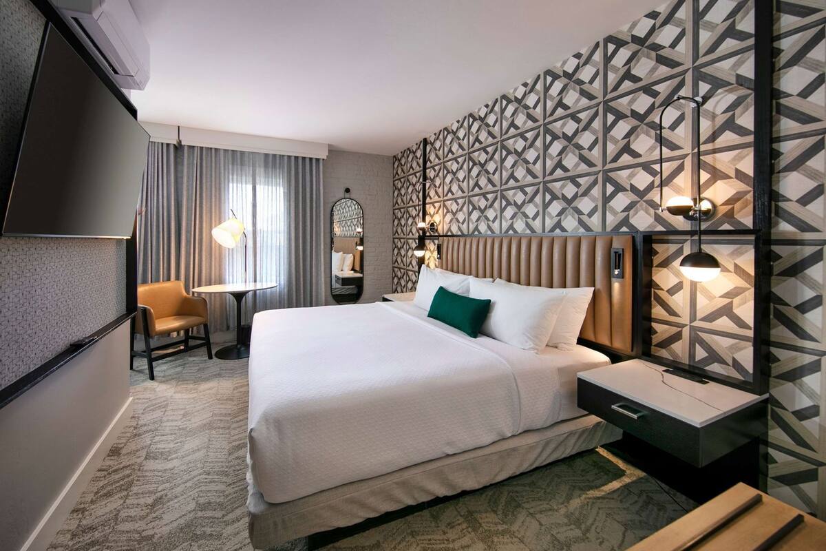 Ein Hotelzimmer mit einem Bett, einem Schreibtisch, einem Stuhl, einem Fernseher und einer Wand mit Muster.