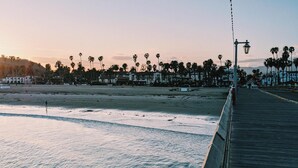 A coastal walkway with a wooden deck, palm trees, and a clear sky.