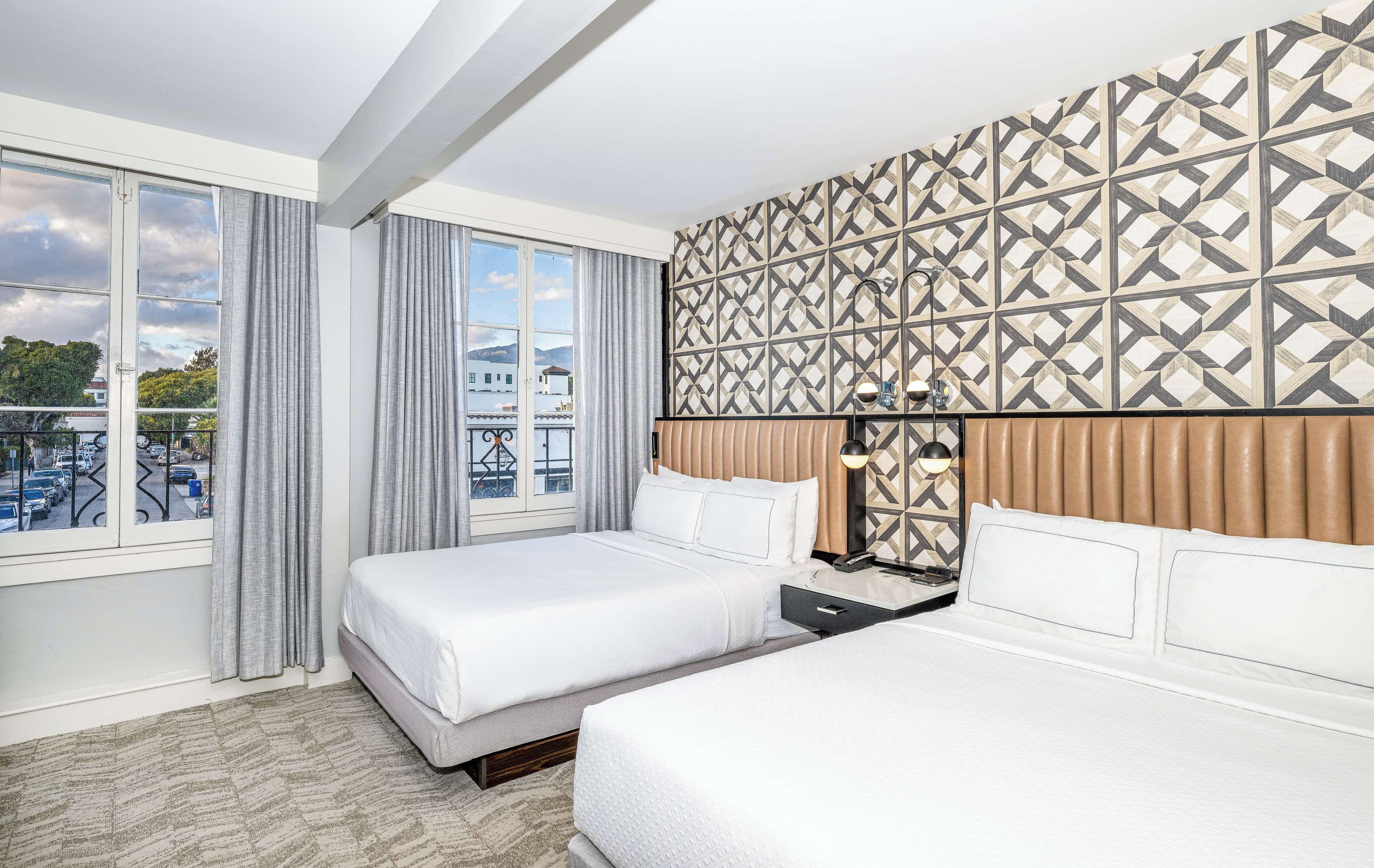 Une chambre d’hôtel avec deux lits, un mur décoré de motifs, une vue sur la ville et un balcon avec une balustrade.