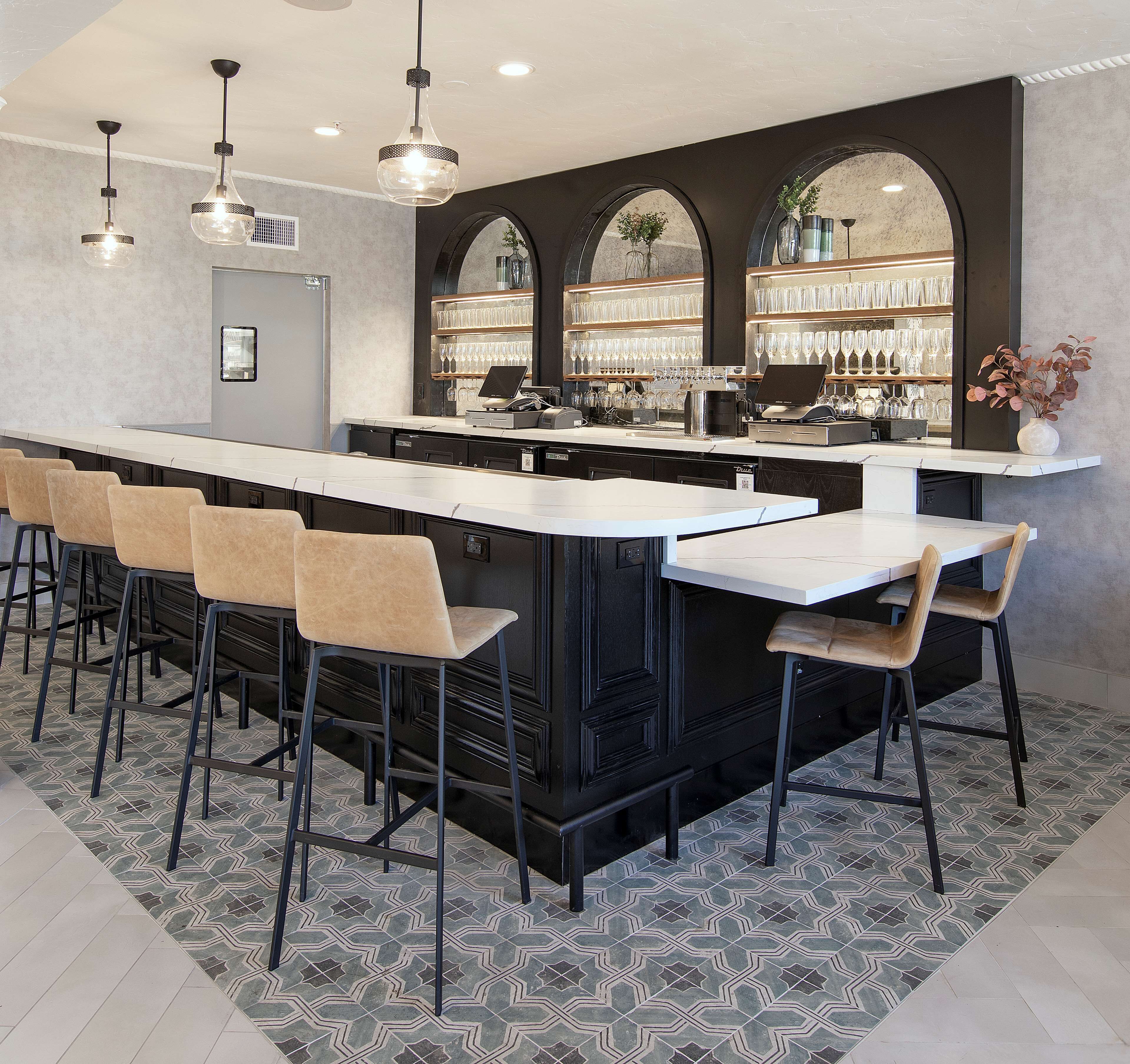 A modern bar area with a long counter, multiple bar stools, and a wine display.
