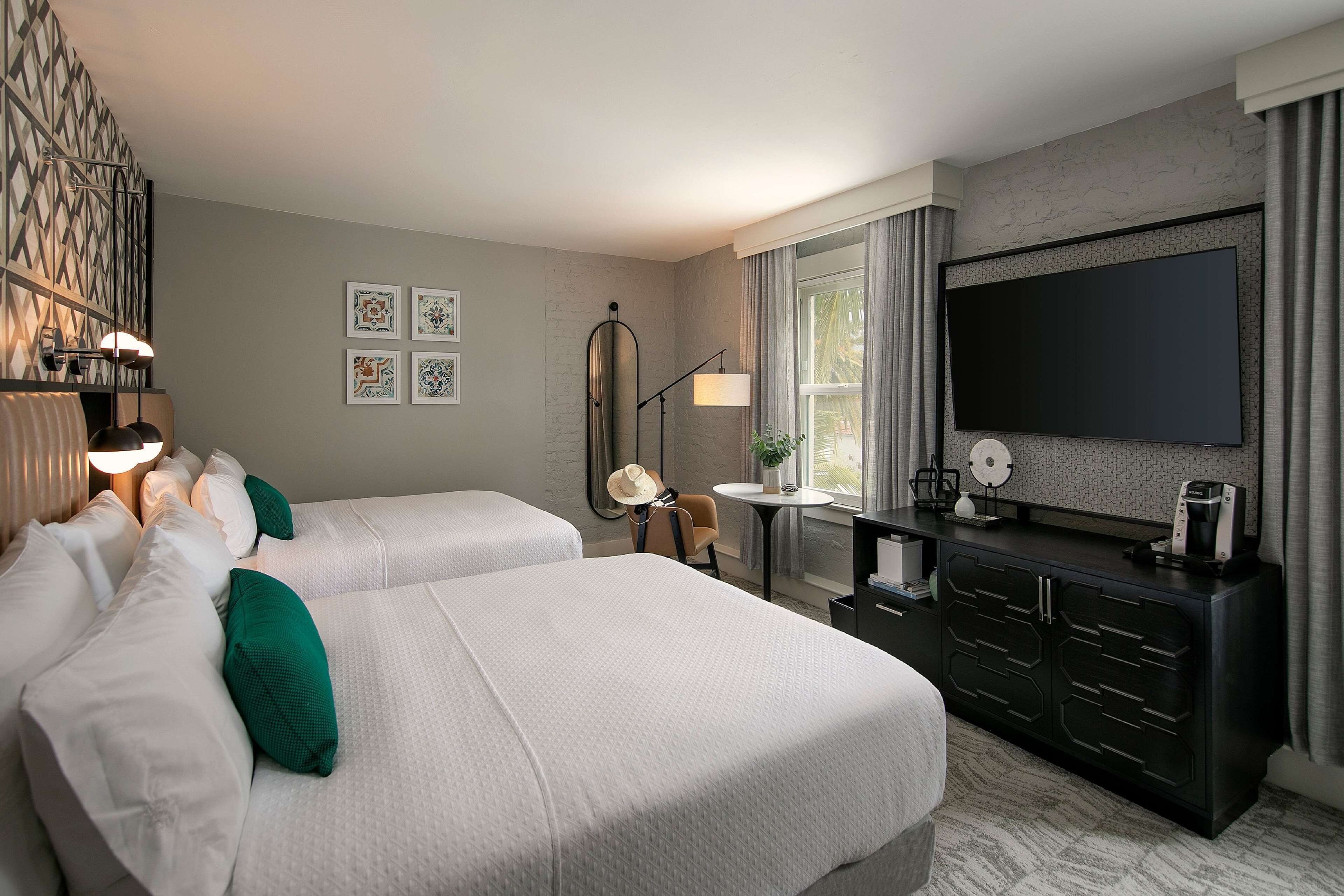 Une chambre d’hôtel avec deux lits, une télévision, un bureau avec une lampe et une fenêtre avec des rideaux.