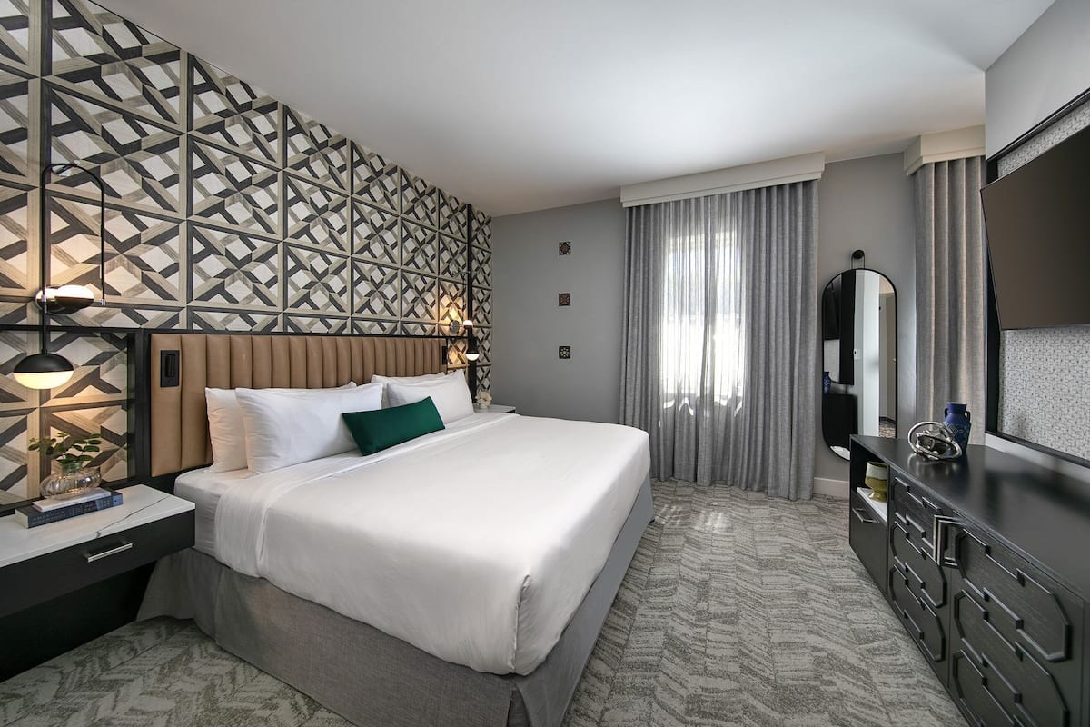 A hotel room with a large bed, a dresser, a mirror, and a geometric-patterned wall.
