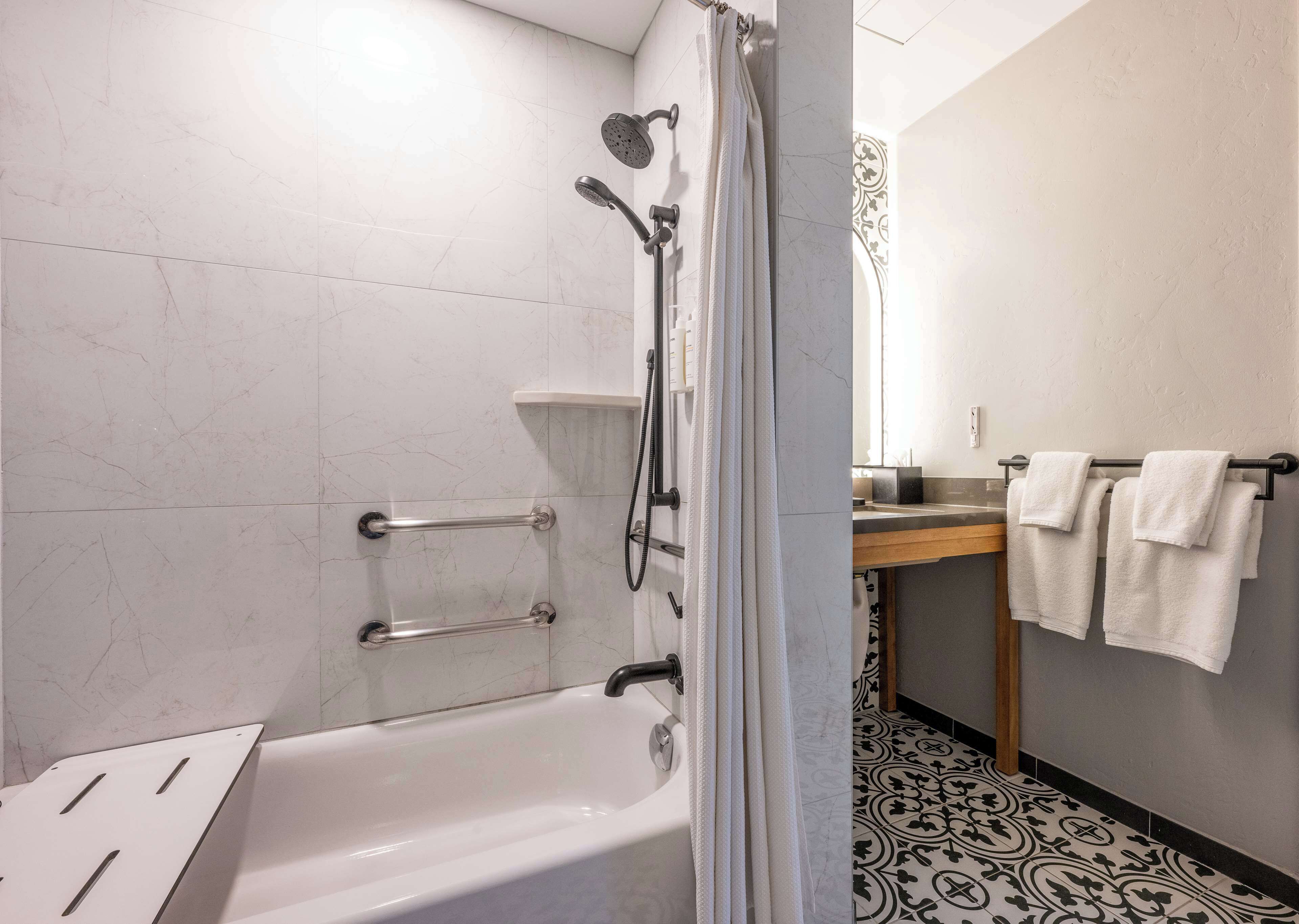 A modern bathroom with a bathtub, shower, and toilet. There are grab bars installed for safety.
