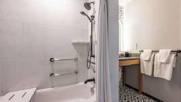A modern bathroom with a bathtub, shower, and toilet. There are grab bars installed for safety.