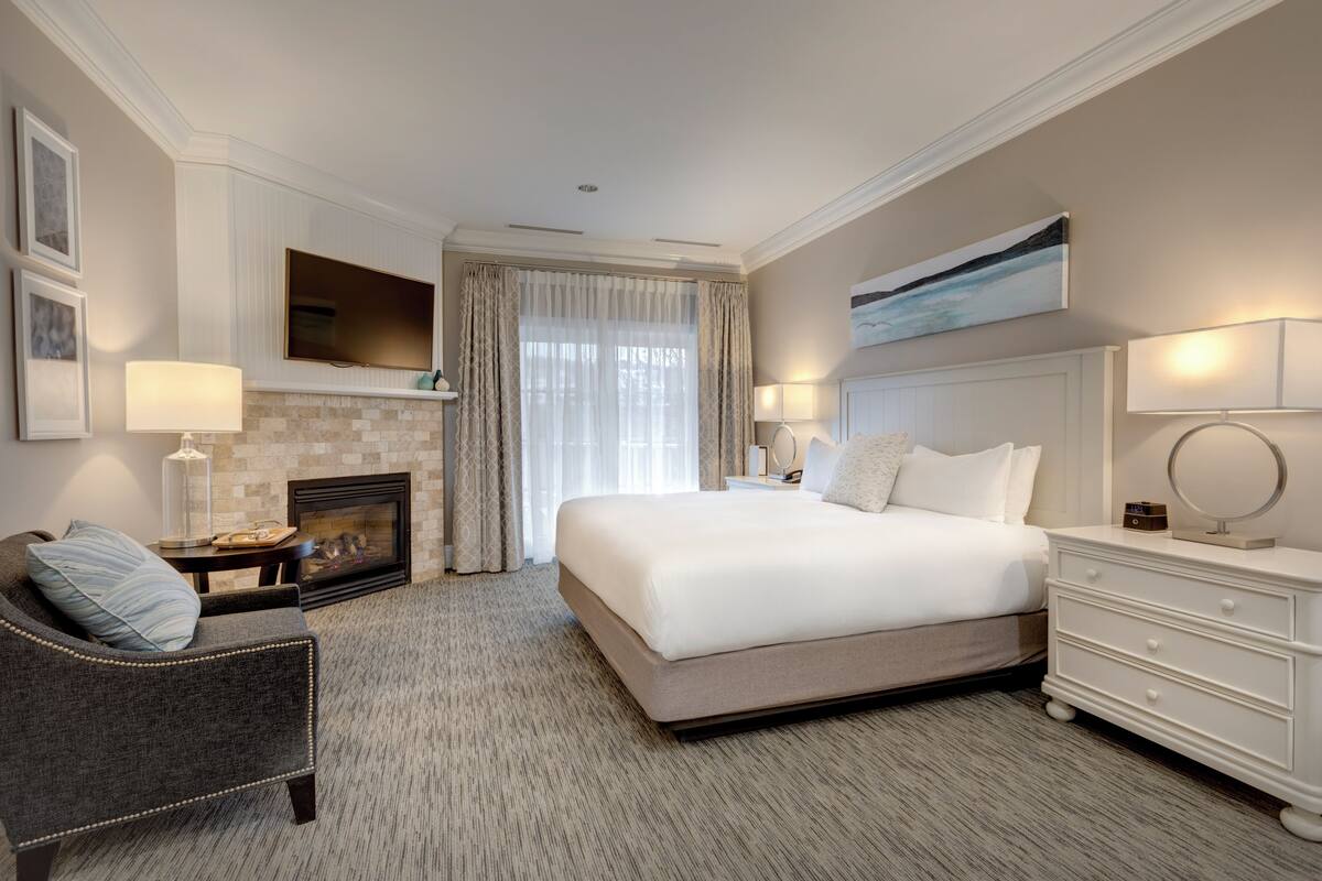 A hotel room with a large bed, a fireplace, a sofa, and a TV mounted on the wall.