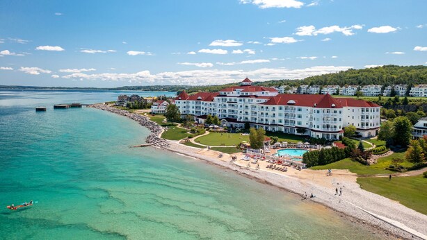 A large hotel with multiple floors, a swimming pool, and a beach area.