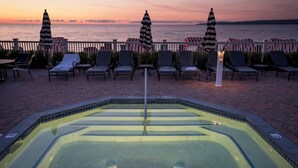 A poolside area with lounge chairs and umbrellas, a pool, and a view of the sea at sunset.
