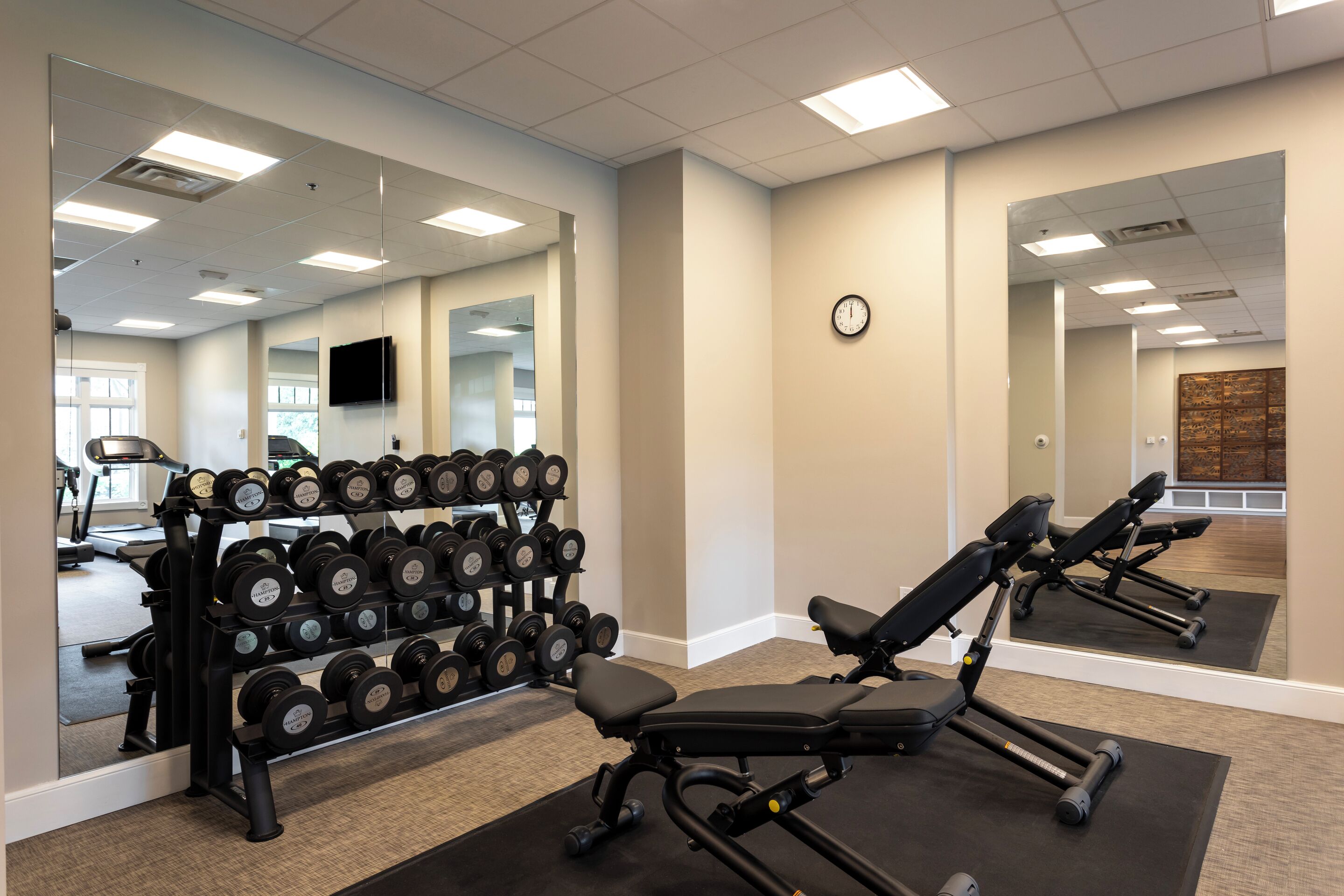 Une salle de sport équipée de matériel d’exercice, avec un miroir et une horloge au mur.