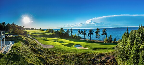 A golf course with a water body in the background, a clear sky, and a well-maintained landscape. - Inn at Bay Harbor (Petoskey)