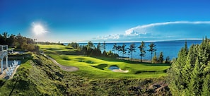 A golf course with a water body in the background, a clear sky, and a well-maintained landscape.