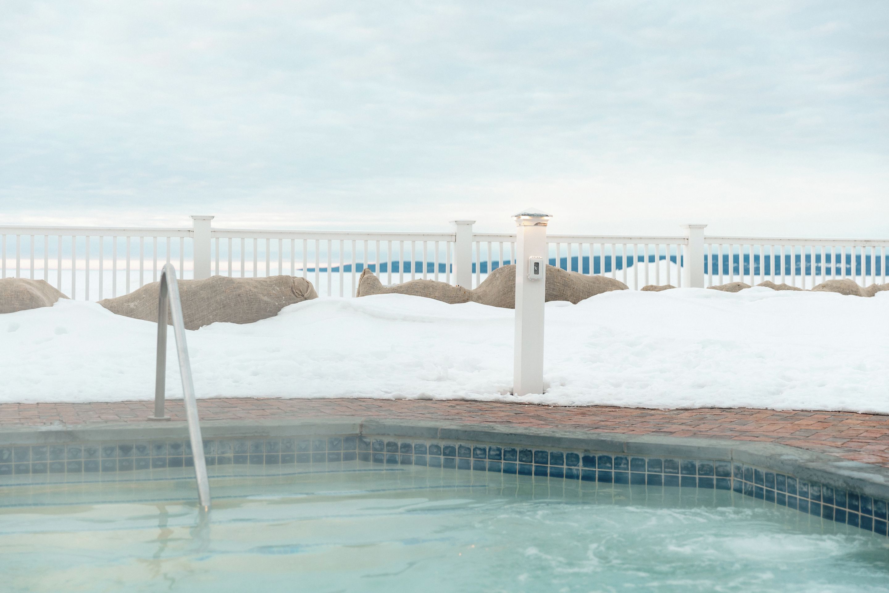 A swimming pool with a white fence and rocks in the background.