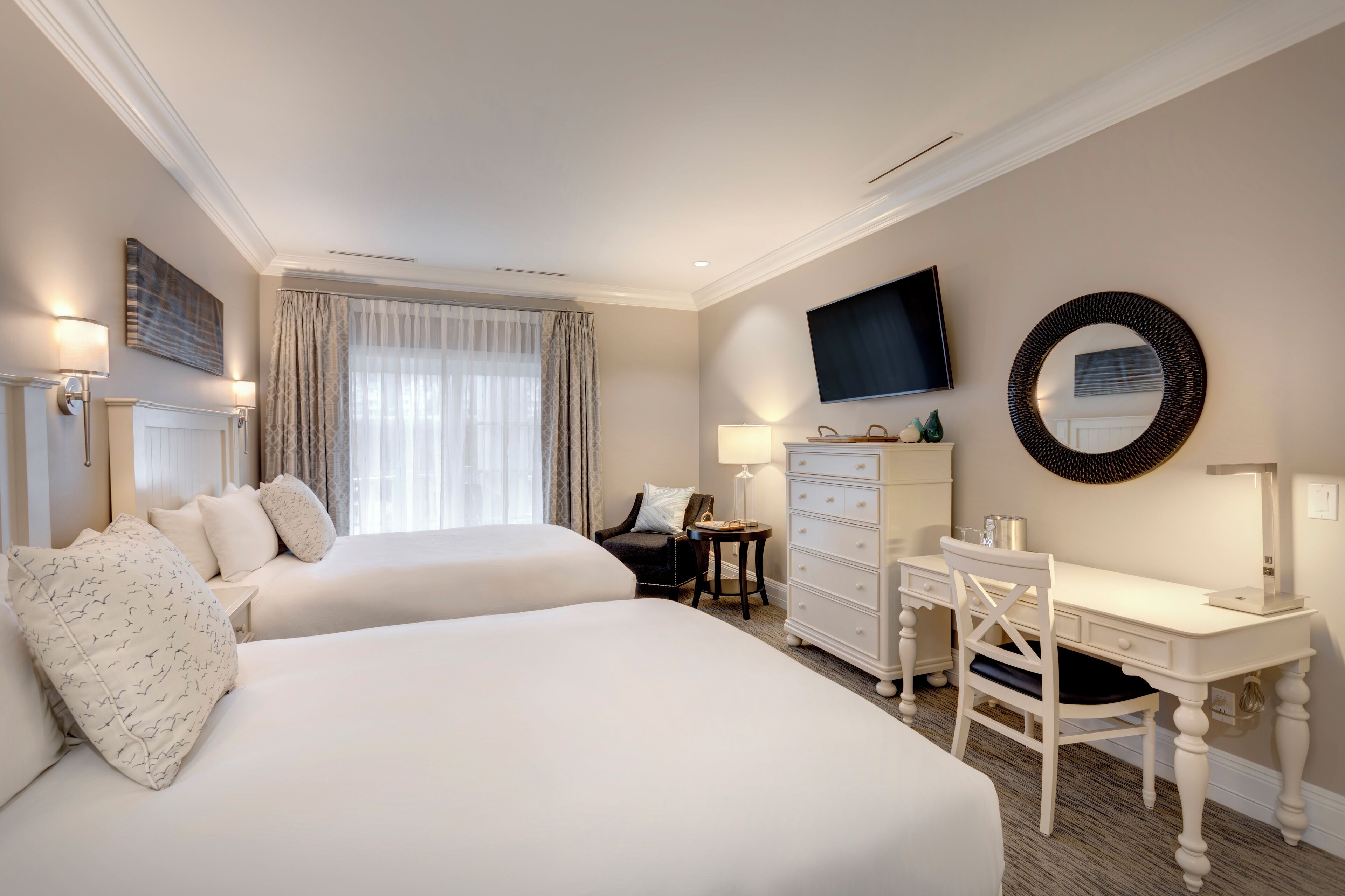 A hotel room with two beds, a desk, a chair, a TV, and a dresser.