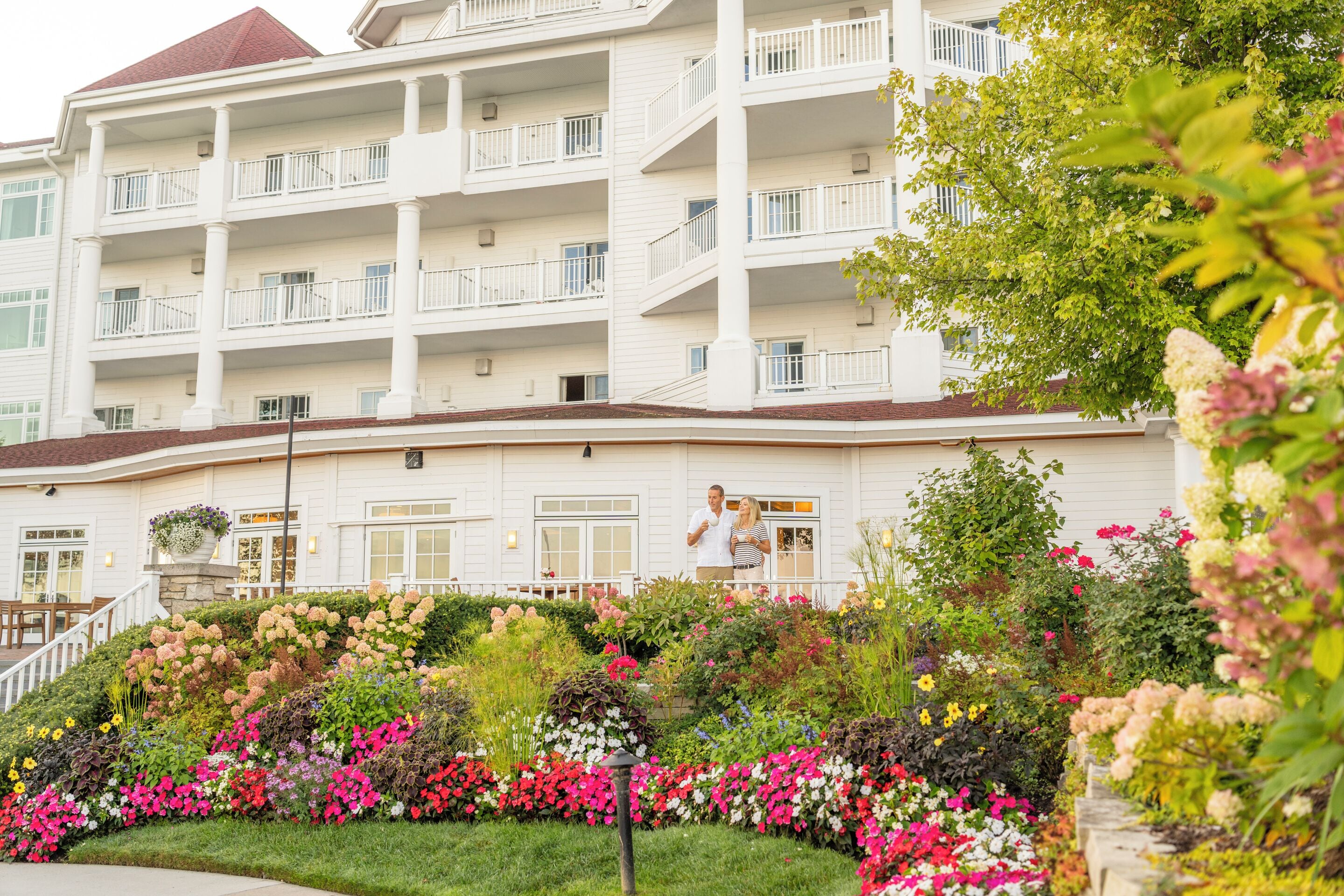 A multi-story hotel with balconies, a landscaped garden with various flowers, and a well-maintained exterior.