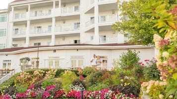 A multi-story hotel with balconies, a landscaped garden with various flowers, and a well-maintained exterior.