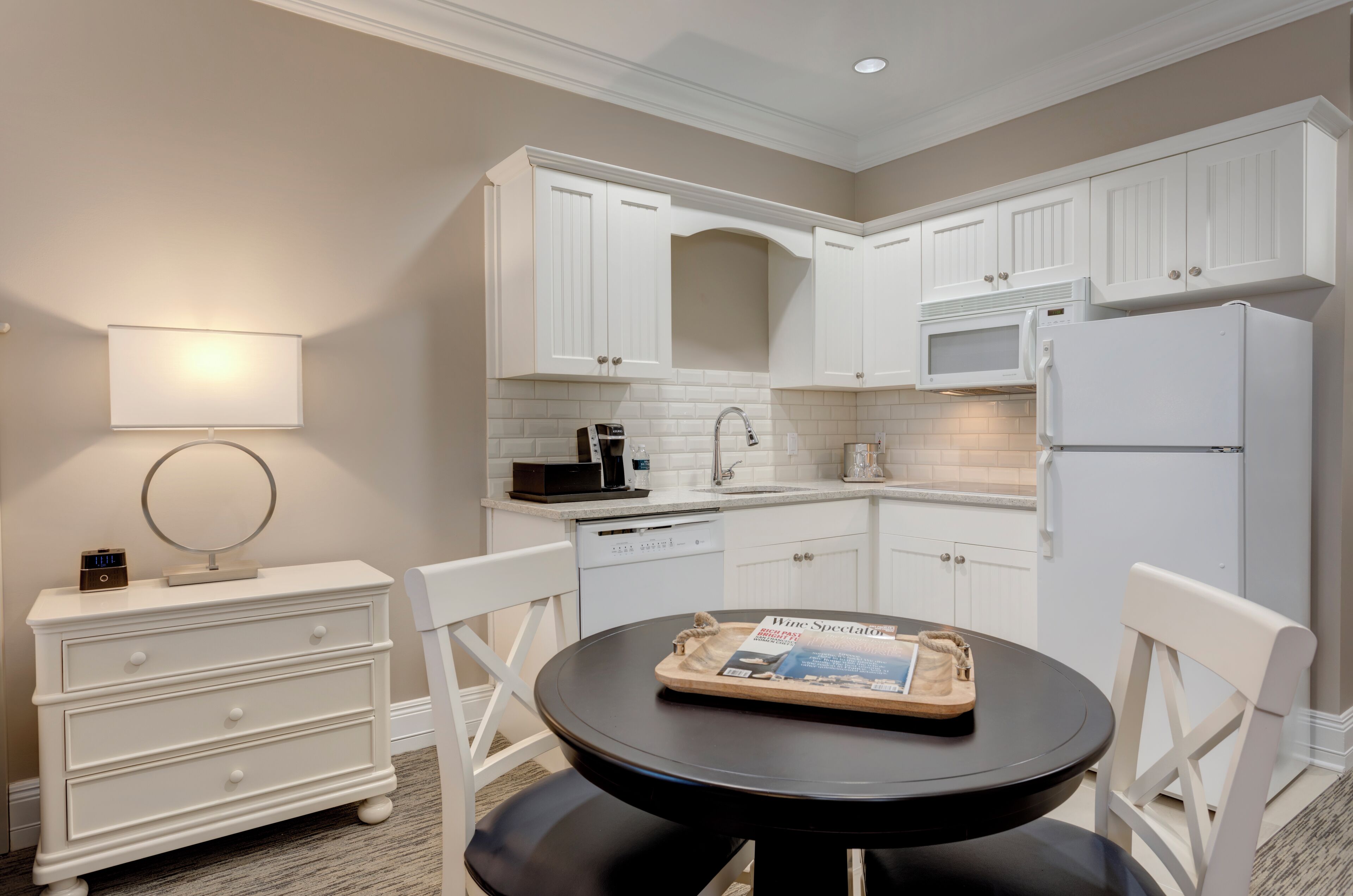 A modern kitchen with white cabinetry, a round dining table, and a magazine on the table.