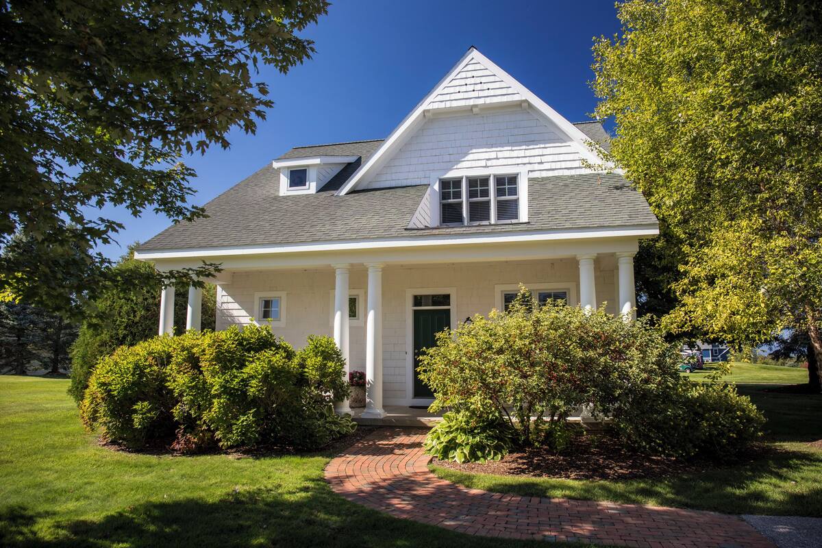 A two-story house with a gabled roof, a front porch with columns, and a green door.