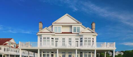 A large, two-story white building with a balcony, a covered front porch, and a brick chimney.