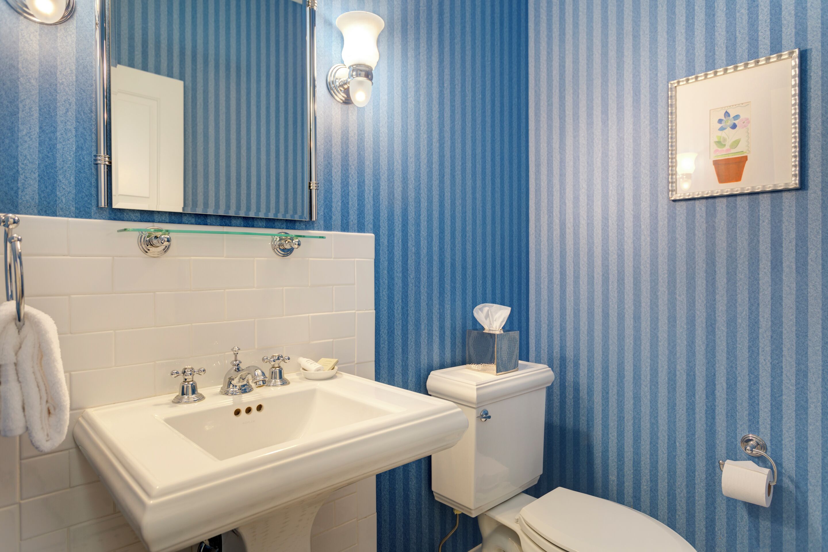 A bathroom with a white sink, mirror, toilet, and blue-striped walls.