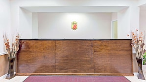 A reception desk with a wooden finish, a logo on the wall, and two vases with dried plants on either side. - Super Inn & Suites Carrollton,West Georgia (Carrollton)