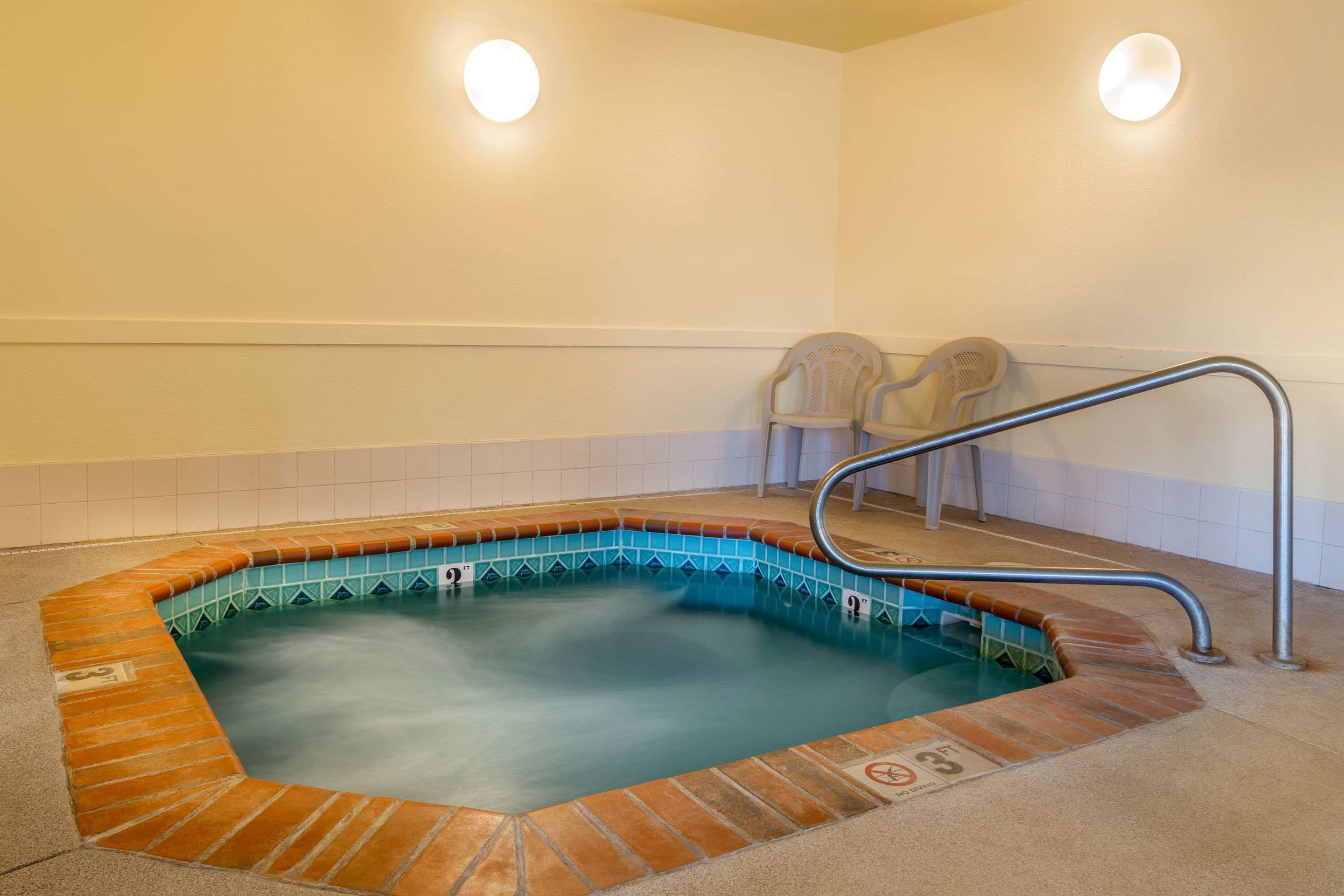 Ein Whirlpool mit Fliesenrand, einer Metallleiter und zwei Stühlen.