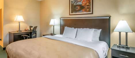 A hotel room with a large bed, two bedside tables with lamps, a desk with a chair, and a painting on the wall.