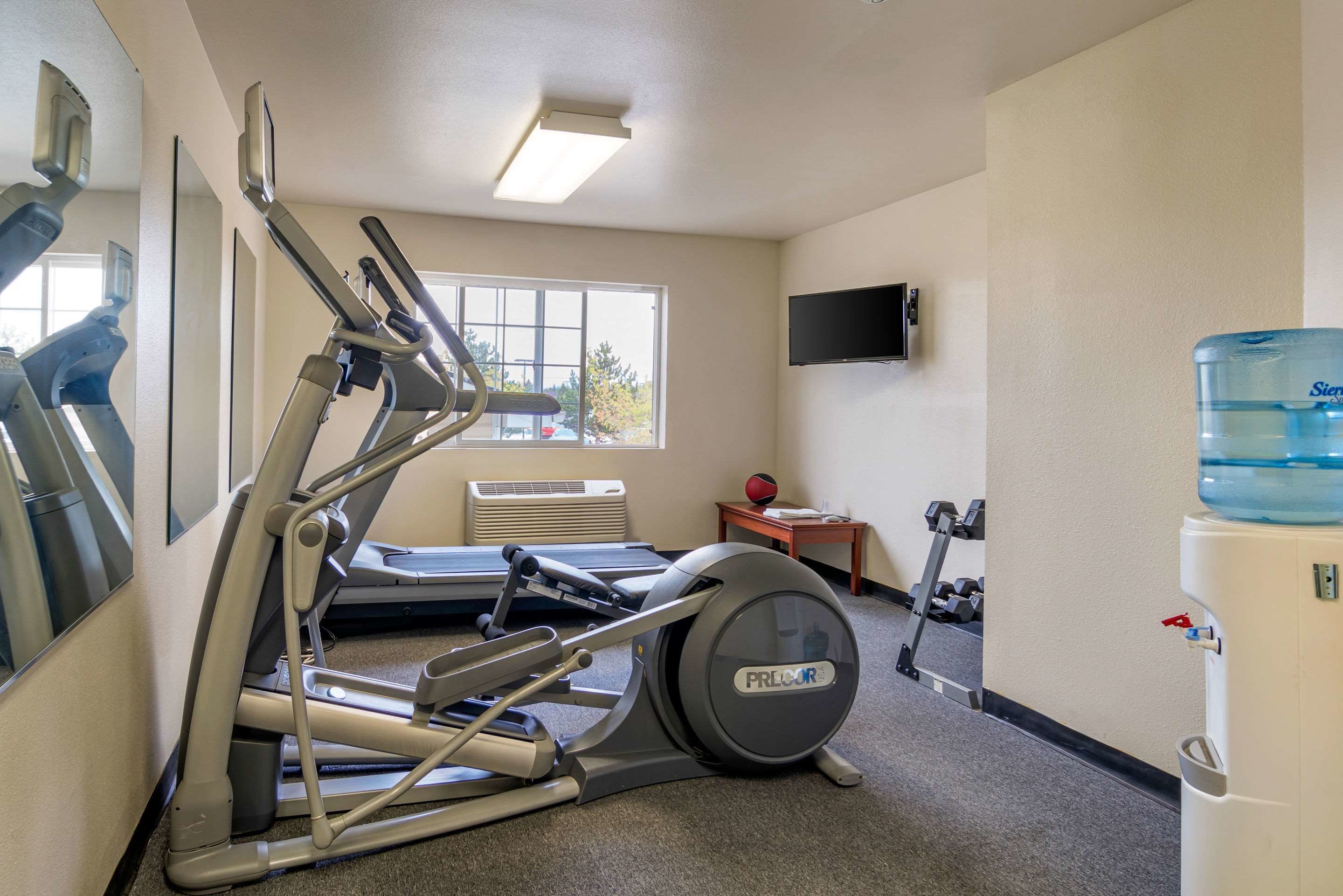 Un gimnasio con equipo cardiovascular, un dispensador de agua y un televisor en la pared.