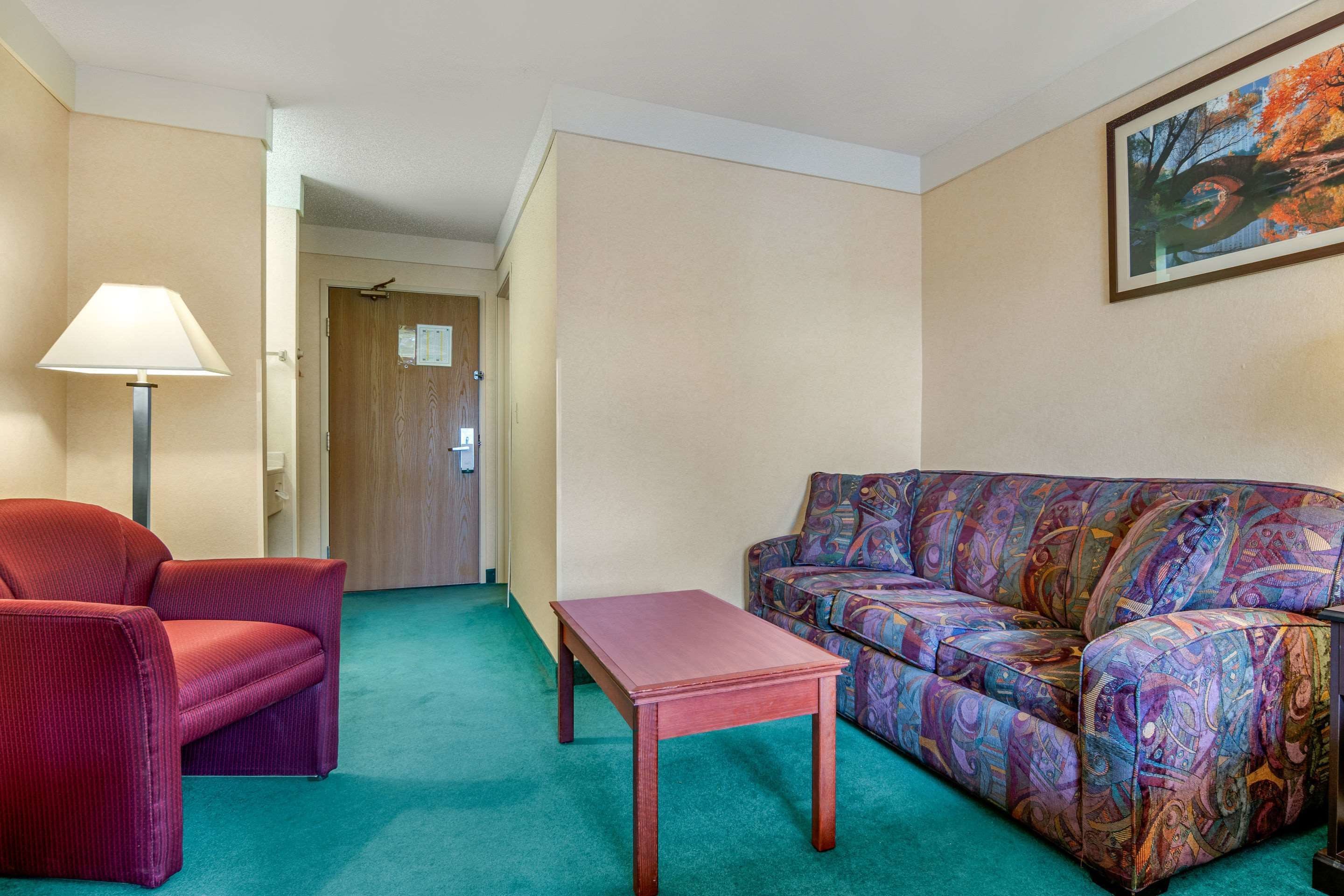 A room with a red armchair, a patterned sofa, a small wooden table, and a lamp.