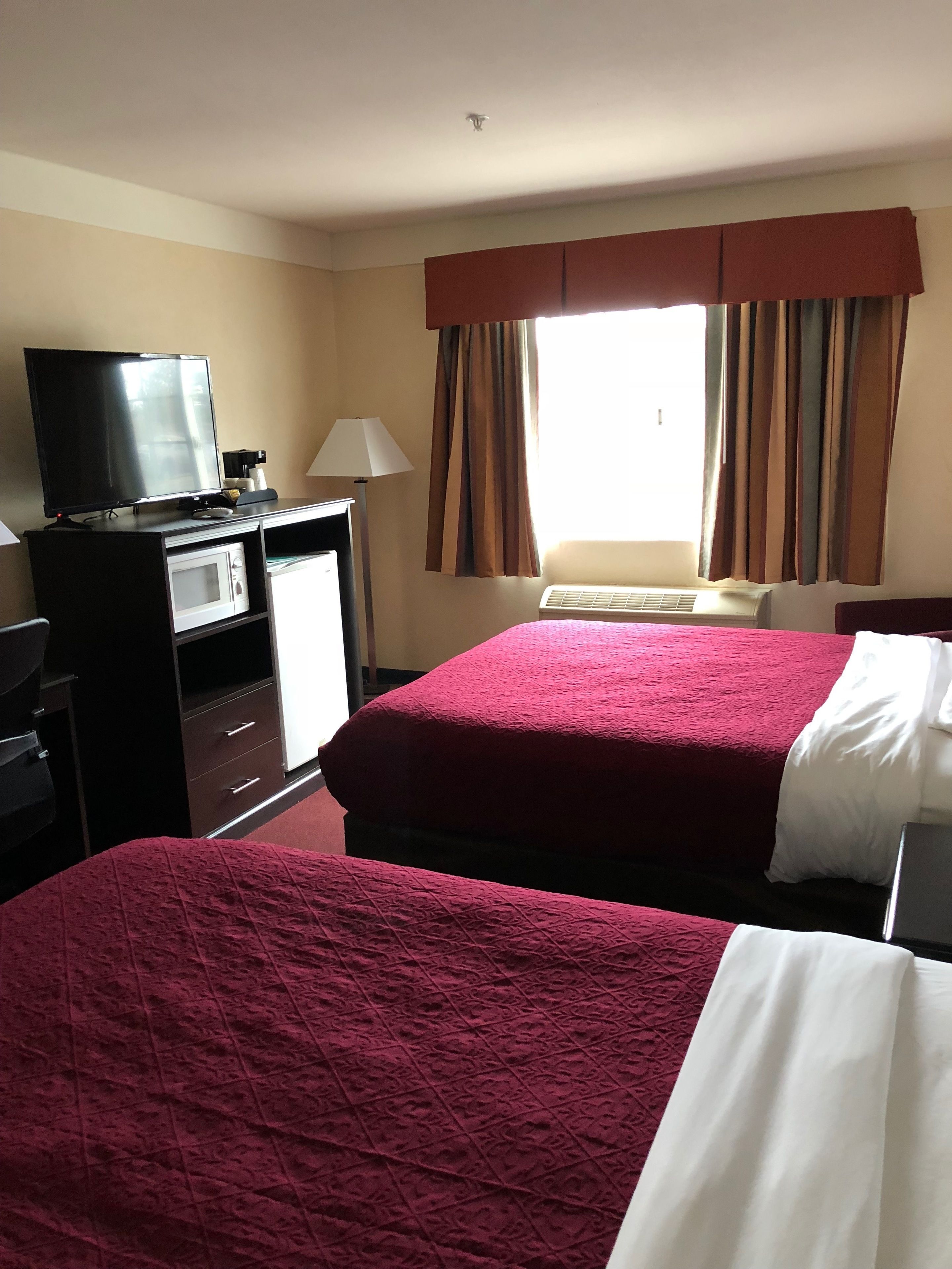 A hotel room with two beds, a TV, a desk with a lamp, and a window with curtains.