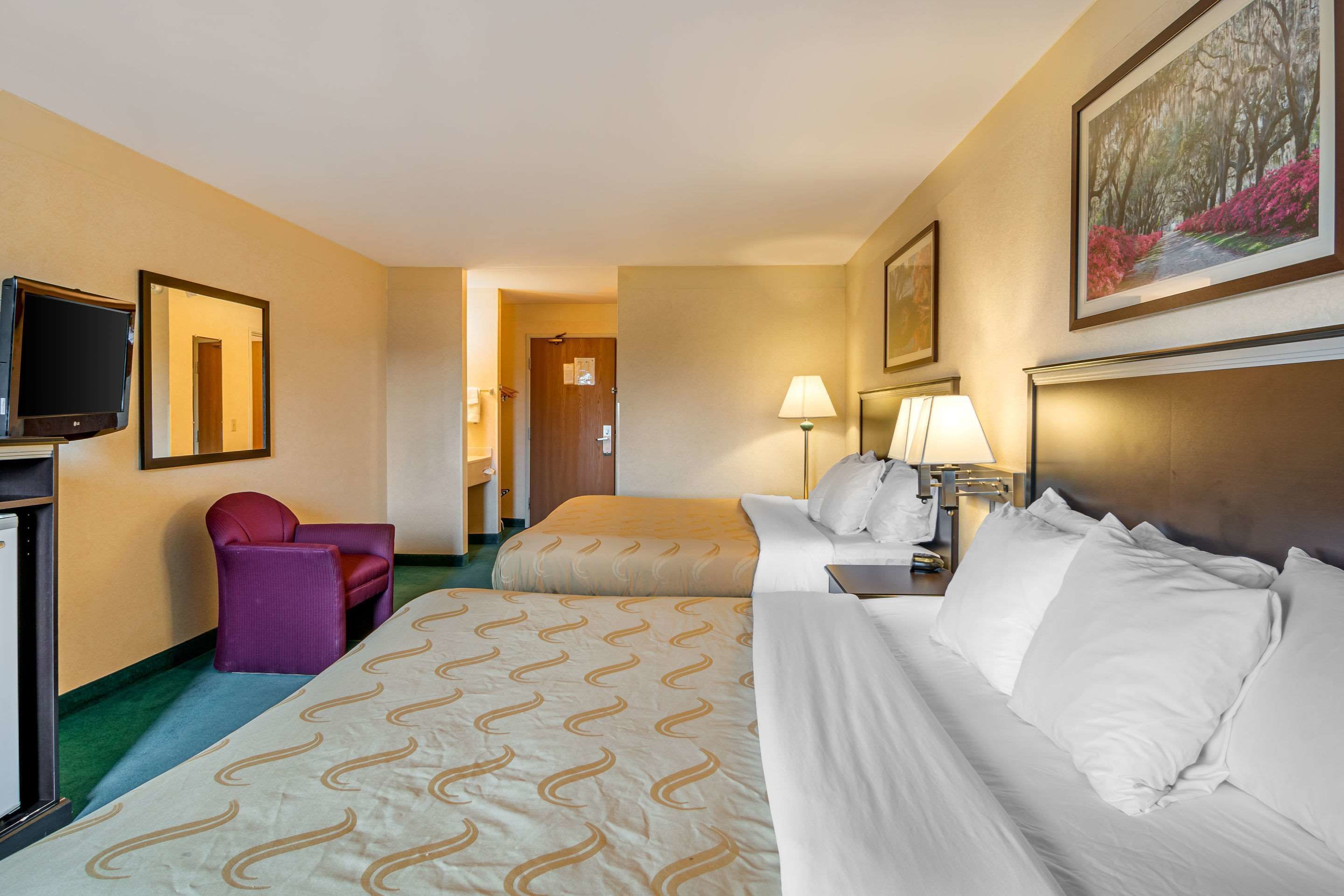 A hotel room with two beds, a TV, a chair, and a painting on the wall.