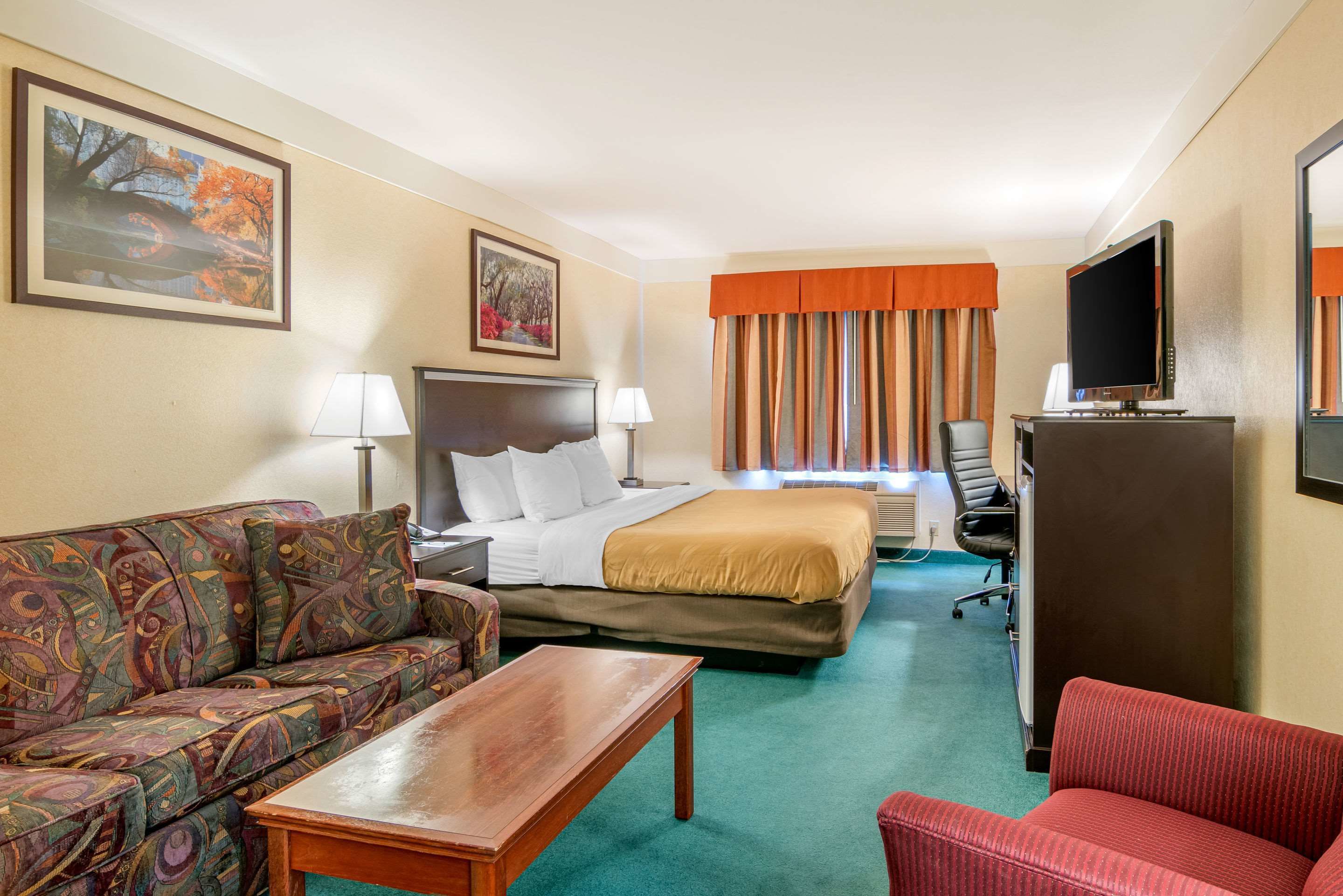 A hotel room with a bed, a sofa, a desk, a TV, and a window with curtains.