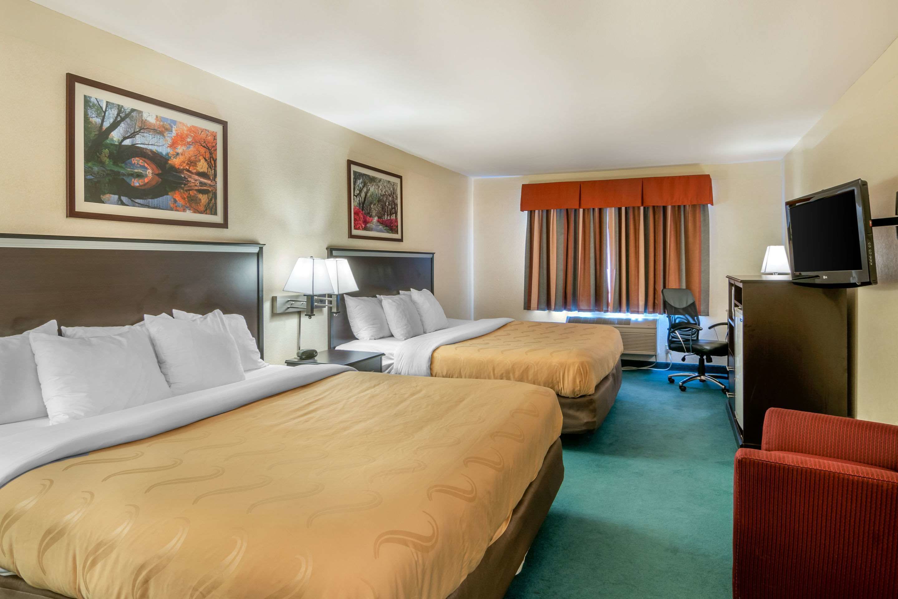 Habitación de hotel con dos camas, un escritorio, una silla, un televisor y una ventana con cortinas.