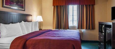 A hotel room with a bed, a nightstand, a lamp, a window with curtains, and a television.