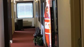 A hotel corridor with a red carpet, vending area sign, exit signs, and a Coca-Cola vending machine.