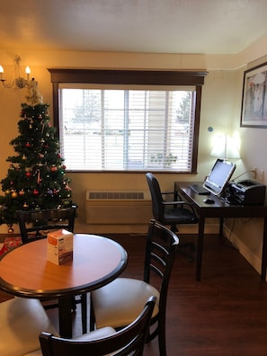 Une pièce comprenant une table à manger, des chaises, un sapin de Noël, un bureau avec un ordinateur et une fenêtre avec des stores.