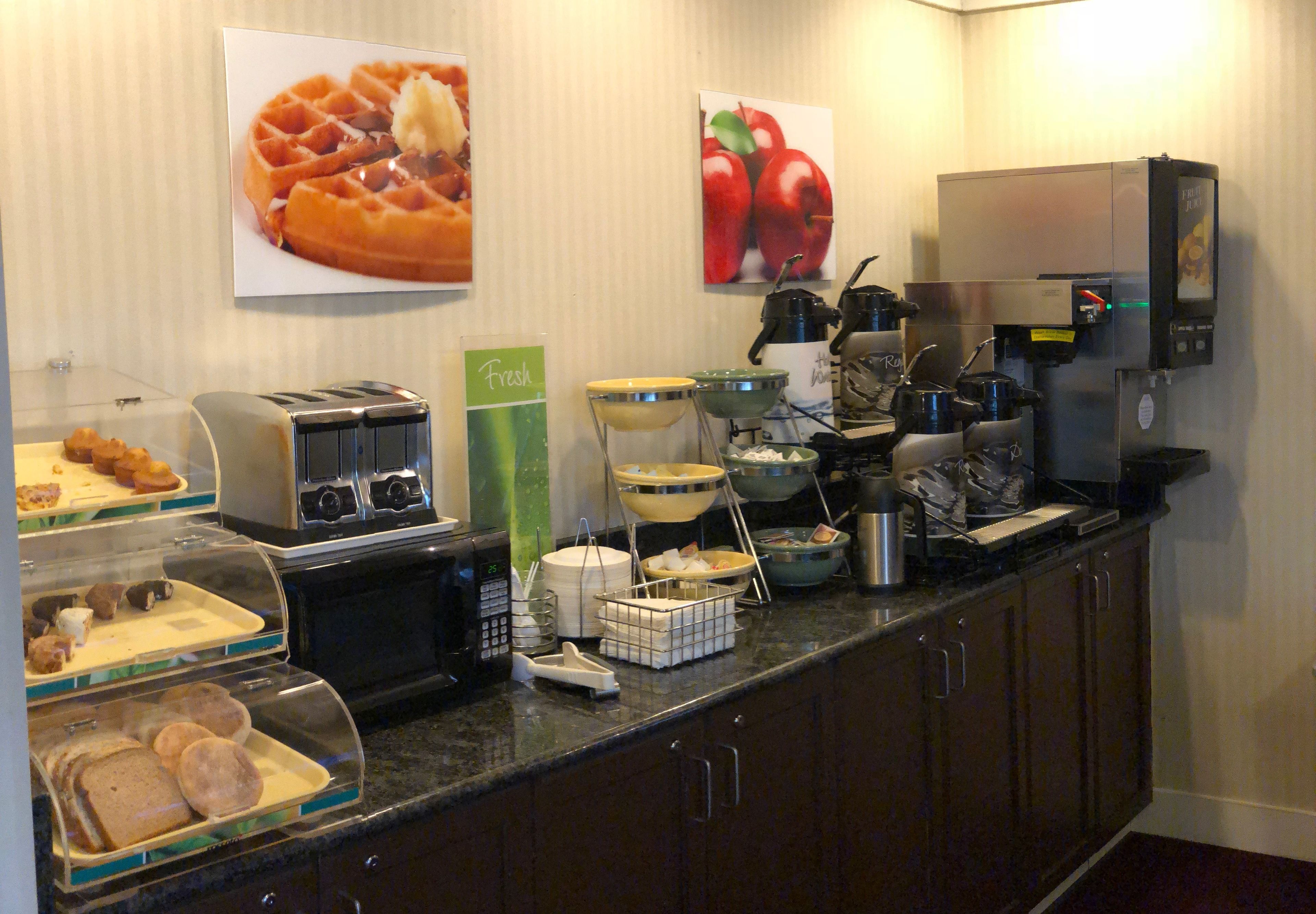 Zona de bufé con diferentes opciones de comida, una máquina de café y una presentación de gofres.