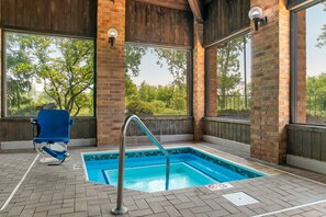 An outdoor swimming pool with a metal ladder, surrounded by brick walls and large windows.