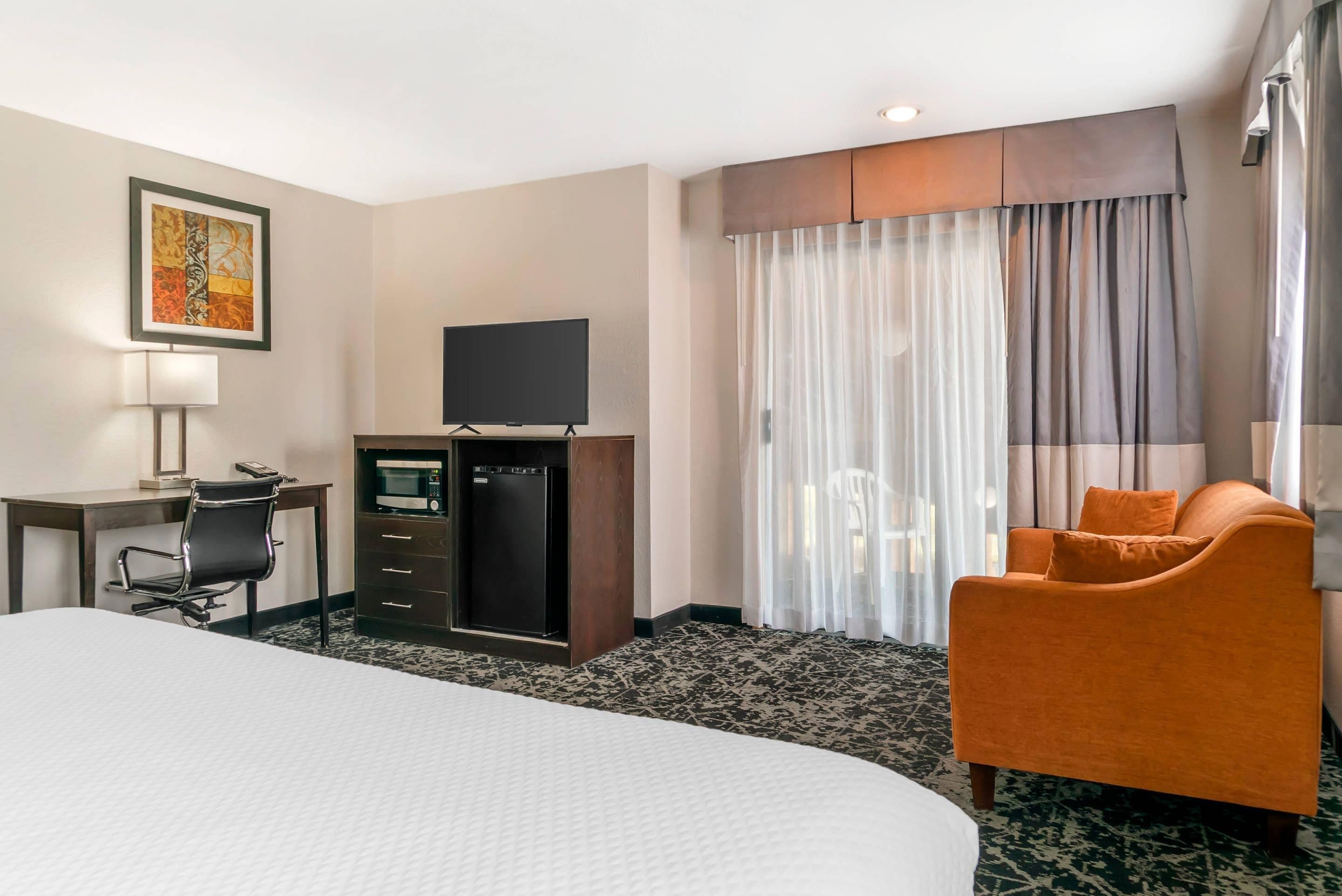 Et hotelværelse med en stor seng, et skrivebord med stol, et fjernsyn, minibar og et vindue med gardiner.