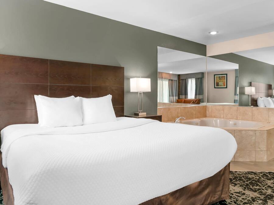 A hotel room with a large bed, a bathroom with a bathtub, and a mirror reflecting the room.