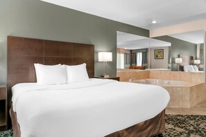 A hotel room with a large bed, a bathroom with a bathtub, and a mirror reflecting the room. - Quality Inn Grand Rapids South-Byron Center (Grand Rapids)