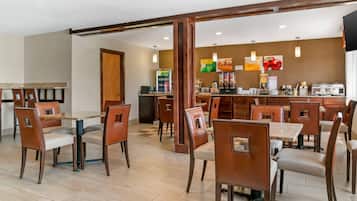 Un comedor de hotel con varias mesas y sillas, una estación de café y una pared decorada con imágenes de frutas.