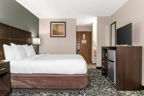 A hotel room with a bed, a desk, a television, and a door leading to a bathroom.
