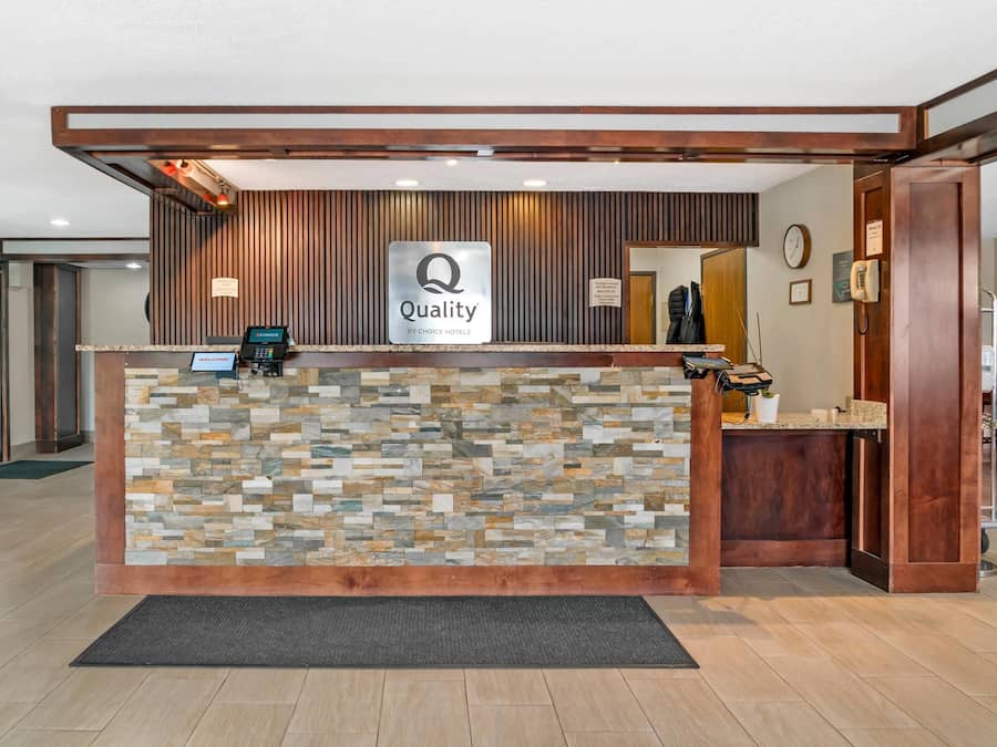 A reception desk with a 'Quality by Choice Hotels' sign, a digital check-in kiosk, and a wooden reception area.