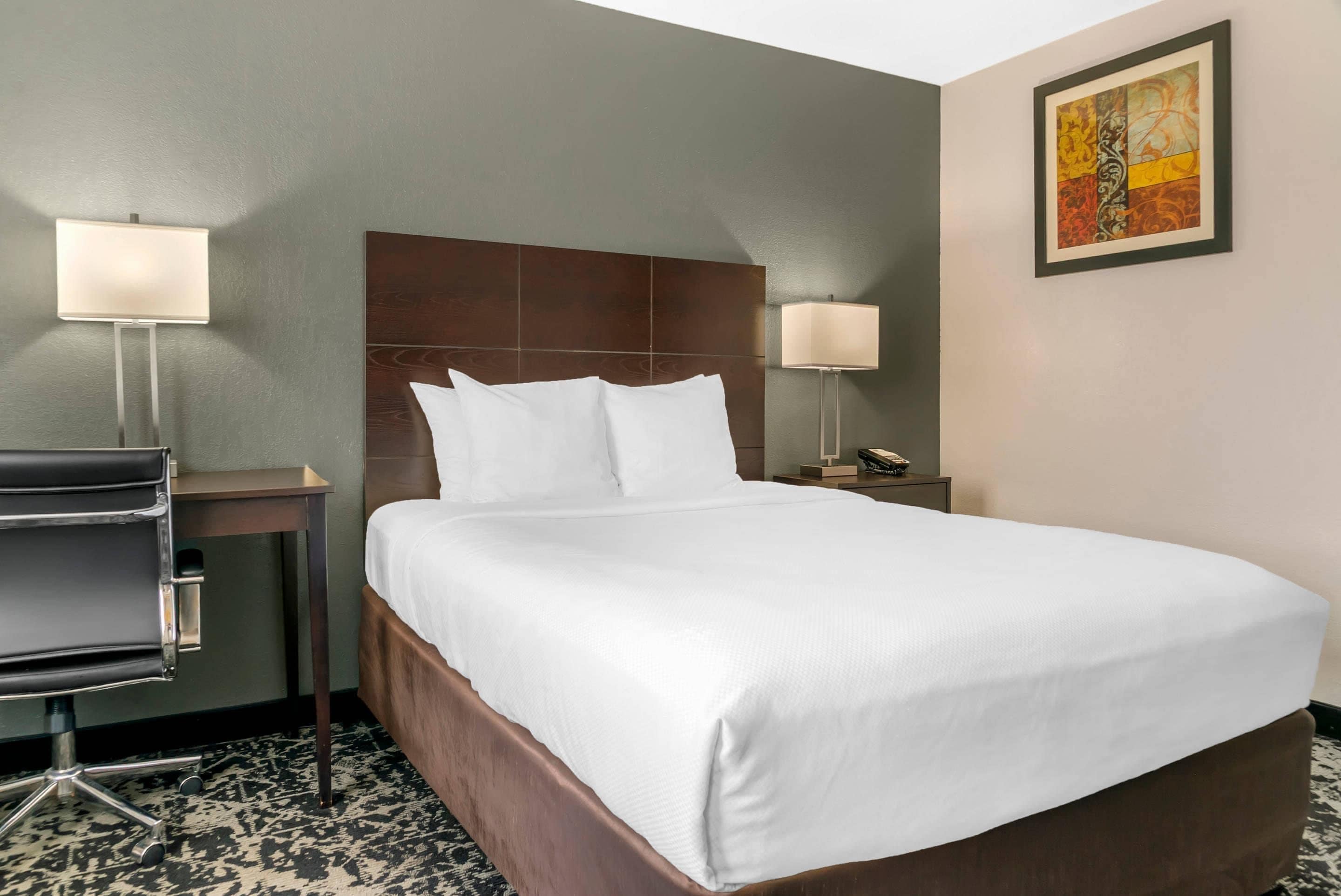 A hotel room with a large bed, two bedside tables with lamps, a desk with a chair, and a patterned floor.