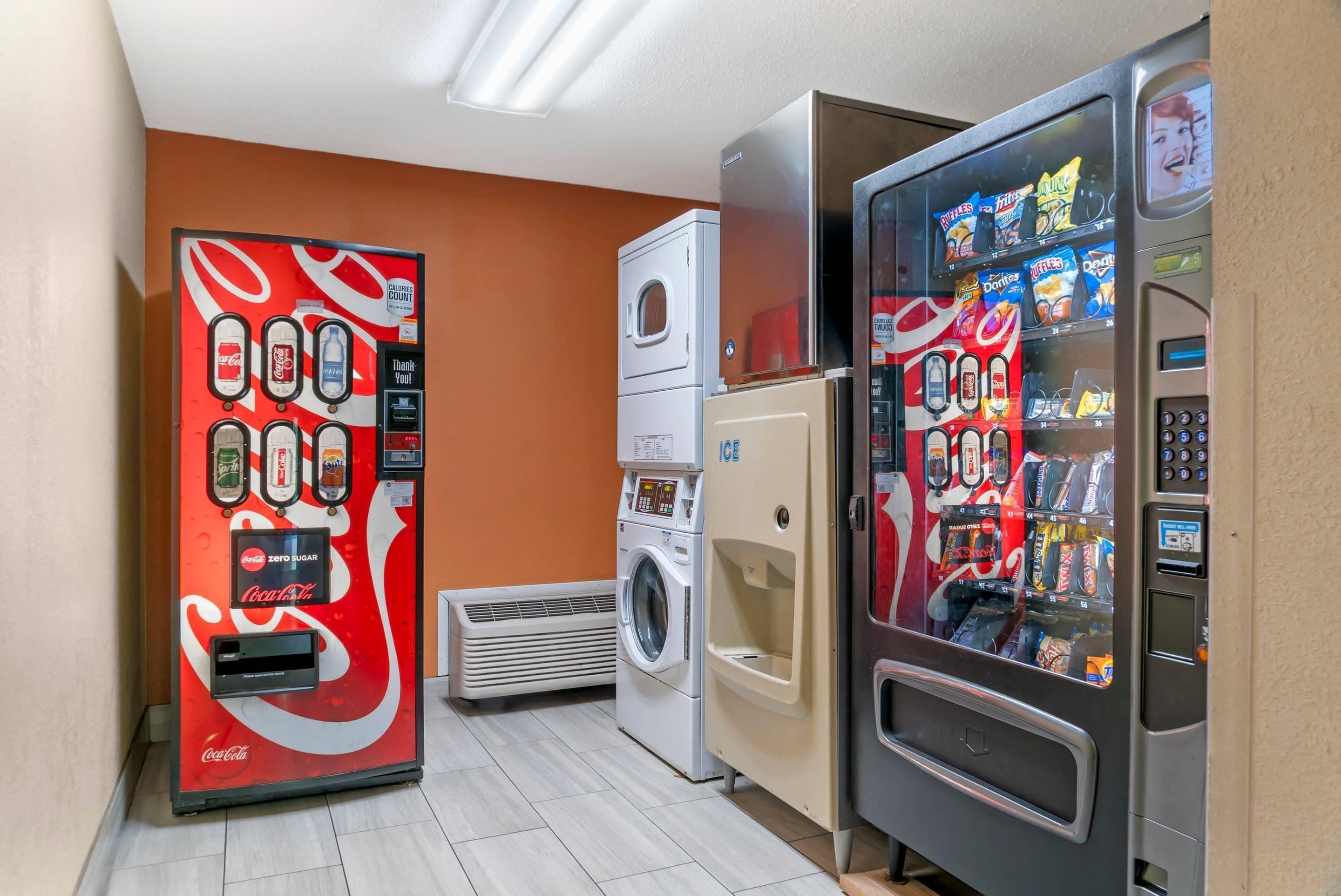 A laundromat with a Coca-Cola vending machine, a washing machine, and a dryer.