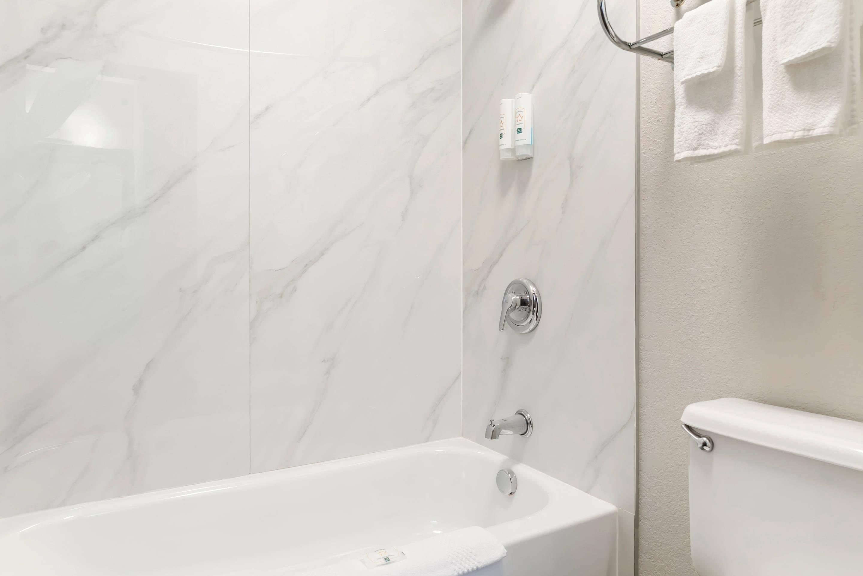 Un baño moderno con pared de mármol, una bañera blanca y un inodoro.