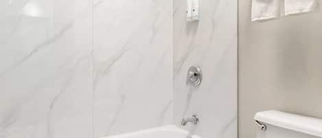 A modern bathroom with a marble wall, a white bathtub, and a toilet.