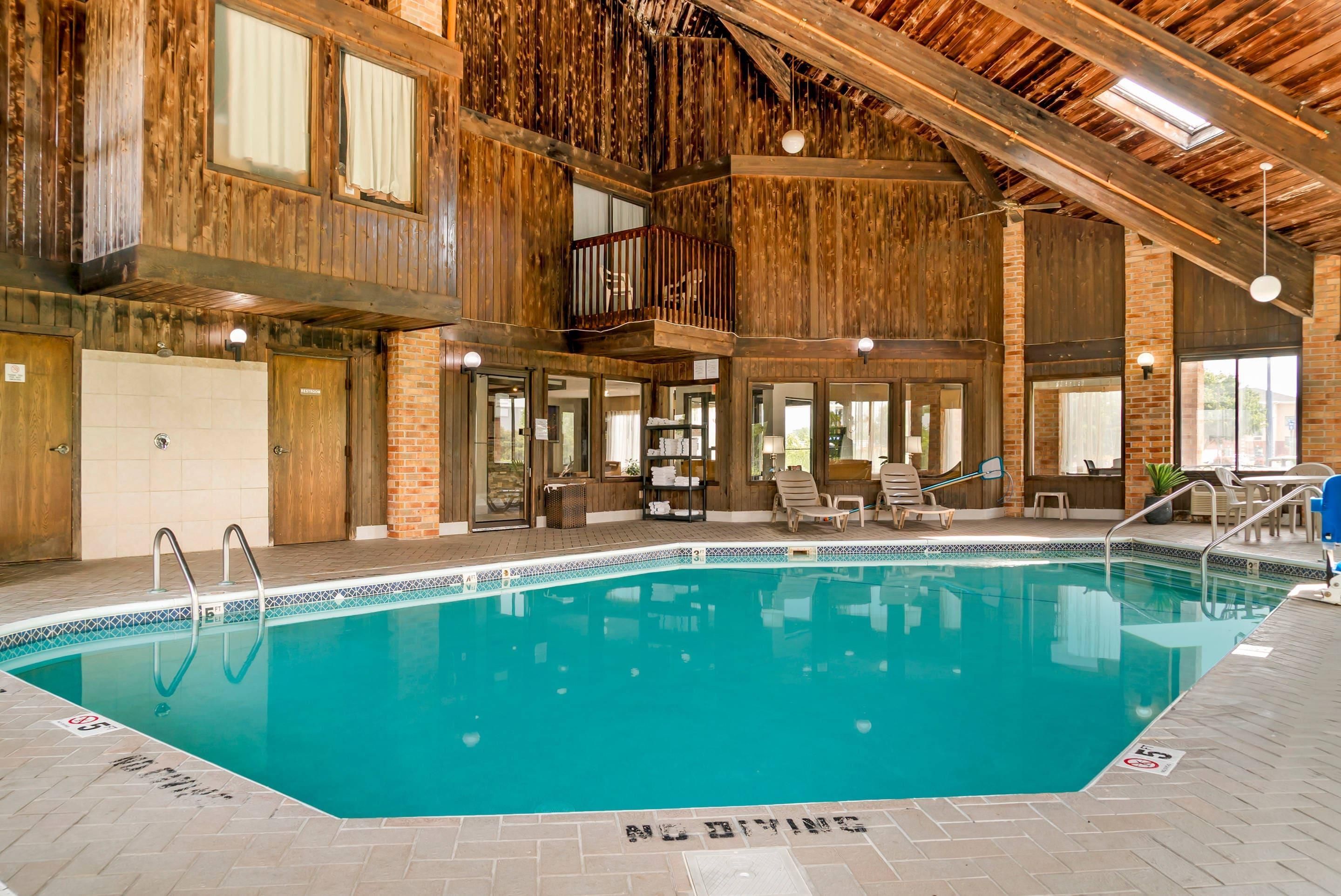 An indoor swimming pool with a wooden interior, a balcony, and a lounge area with chairs and a table.