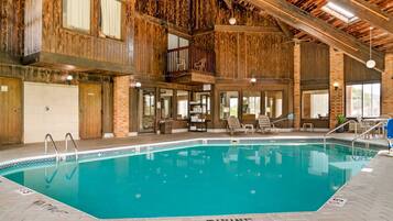An indoor swimming pool with a wooden interior, a balcony, and a lounge area with chairs and a table.